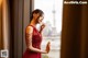 A woman in a red dress standing by a window.