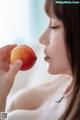 A woman holding a peach in front of her face.