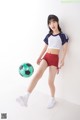 A young woman kicking a soccer ball in a white room.