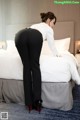 A woman in a white shirt and black pants standing on a bed.