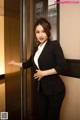 A woman in a black suit standing in an elevator.