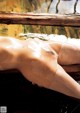 A nude woman laying on a wooden bench in the water.