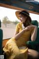 A woman in a yellow dress and hat sitting in the back of a car.