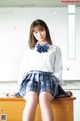 A woman in a school uniform sitting on a desk.