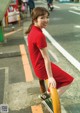 A woman in a red dress leaning on a yellow pole.