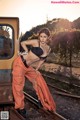 A woman in a black bra top and orange pants posing on a train track.