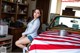 A woman sitting on top of a car covered in an American flag.