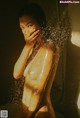 A naked woman standing in a shower with her hands on her face.