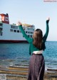 A woman standing on a pier with her arms outstretched in front of a large ship.