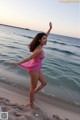 A woman in a pink dress standing on a beach.