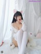 A woman in a white sweater and white stockings sitting on a bed.