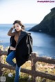 A woman leaning on a wooden fence by the ocean.