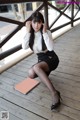 A woman in a white shirt and black skirt sitting on a wooden floor.