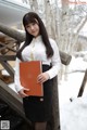 A woman in a white shirt and black skirt holding a book.