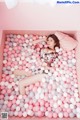 A woman laying in a pink and white ball pit.