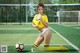 A woman in a yellow shirt and white shorts posing with a soccer ball.