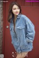 A woman wearing a denim jacket standing in front of a red door.