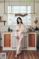 A woman standing in a kitchen wearing a pink pajama set.