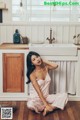 A woman sitting on the floor in a kitchen next to a sink.