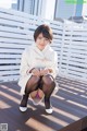 A woman in a white coat and black stockings sitting on a wooden deck.