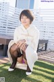 A woman in a white coat and black stockings sitting on a bench.