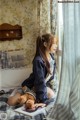 A woman sitting on a bed reading a book with a teddy bear.