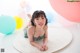 A little girl laying on a white rug with colorful balloons.