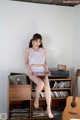 A woman sitting on top of a book shelf next to a guitar.